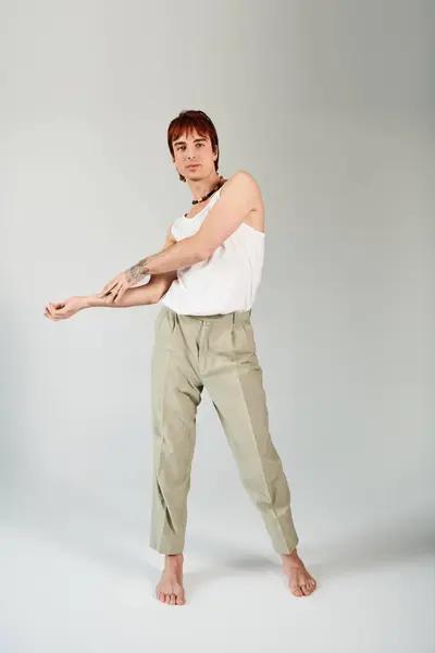 Stilvoller junger Mann posiert im Studio, trägt weißes Tank-Top und khakifarbene Hose vor grauem Hintergrund. — Stockfoto