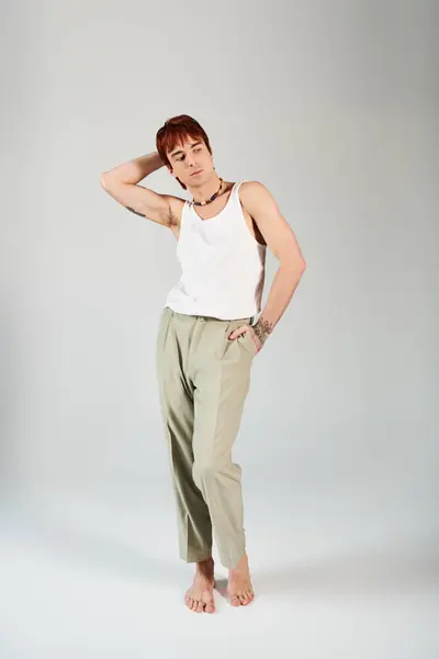 A stylish young man striking a pose in a white tank top and khaki pants against a grey studio background. — Stock Photo