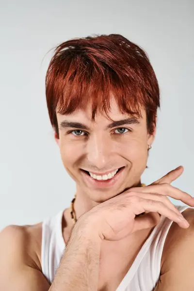 Un jeune homme élégant aux cheveux roux posant avec confiance dans un débardeur blanc sur fond de studio gris. — Photo de stock