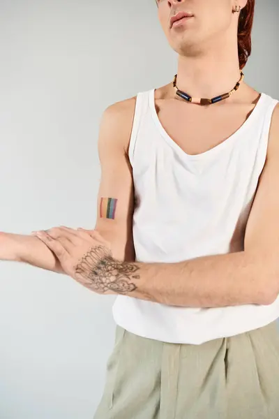A stylish young man striking a pose to showcase a bold tattoo on his arm in a studio against a grey background. — Stock Photo