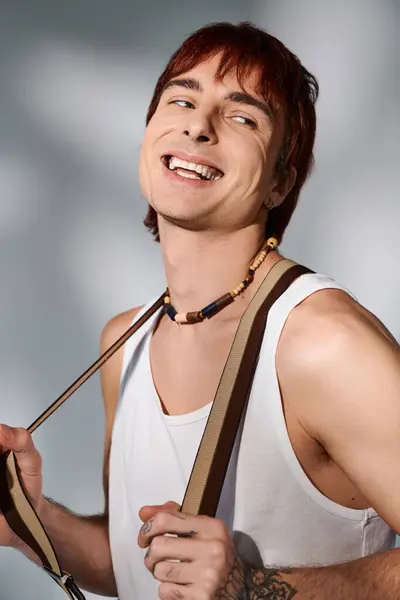 Ein stylischer junger Mann mit roten Haaren posiert in einem Studio und hält eine Kamera vor einem grauen Hintergrund. — Stockfoto