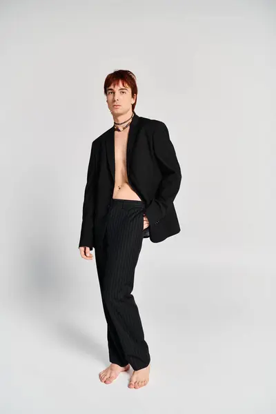 Un joven con estilo en un traje alcanza una pose en un ambiente de estudio con un fondo gris. - foto de stock