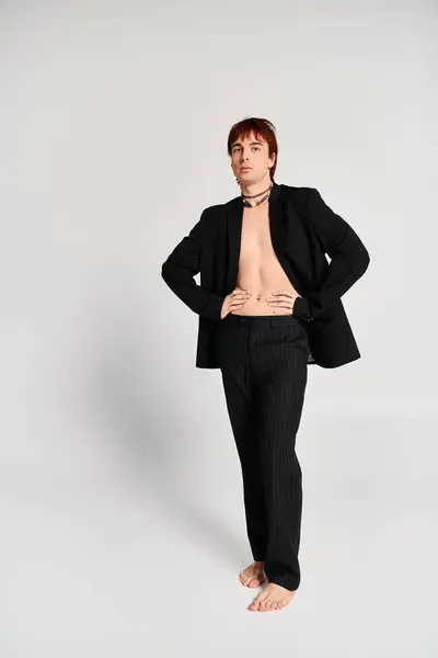 A stylish young man in a suit confidently stands with his hands on his hips in a studio with a grey background. — Stock Photo