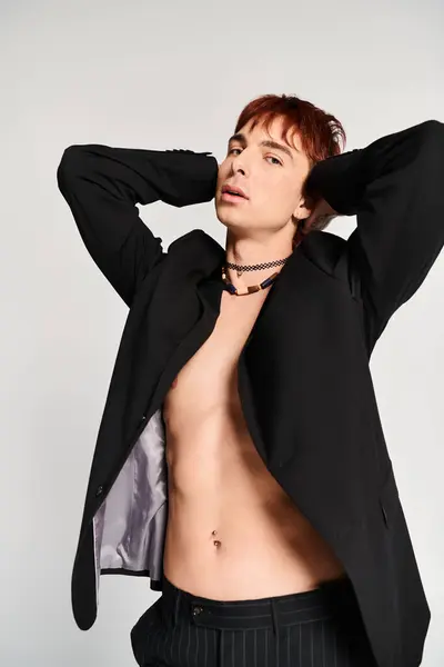 Un giovane elegante, senza maglietta e in completo, posa fiducioso per una foto in uno studio con uno sfondo grigio. — Foto stock