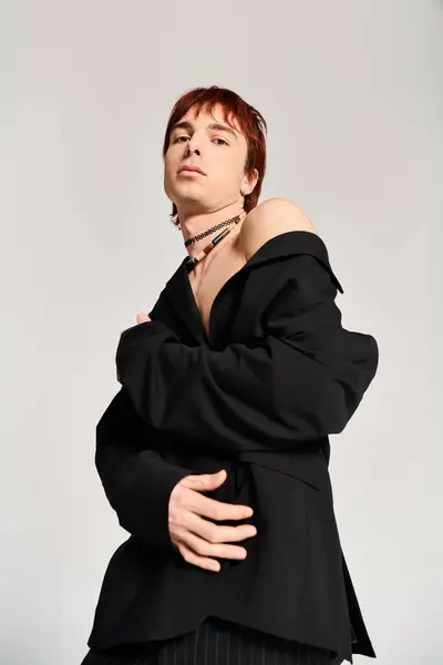 Стильный молодой человек с рыжими волосами уверенно позирует в черной куртке на сером фоне студии. — стоковое фото