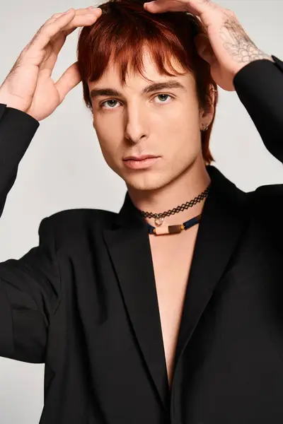 Un jeune homme élégant aux cheveux roux pose avec confiance dans une chemise noire sur un fond de studio gris. — Photo de stock
