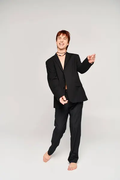Um jovem elegante em um terno preto marcando uma pose confiante contra um fundo de estúdio cinza. — Fotografia de Stock
