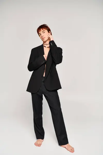 Un joven con estilo posa con un traje elegante contra un fondo gris del estudio. - foto de stock