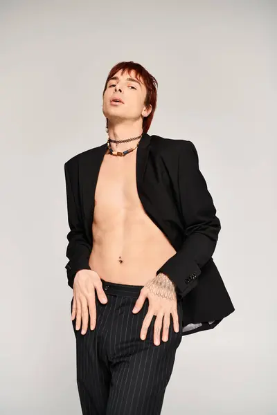 Ein stilvoller junger Mann im Anzug steht selbstbewusst mit offenem Hemd da und posiert in einem Studio mit grauem Hintergrund.. — Stockfoto