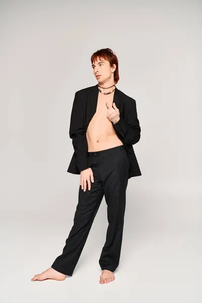 Um jovem elegante posa confiantemente em um estúdio, vestindo um terno, contra um fundo cinza. — Fotografia de Stock