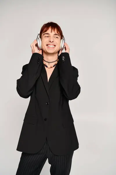 Ein stilvoller junger Mann im Anzug mit Kopfhörern vor grauem Hintergrund. — Stockfoto
