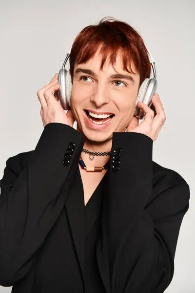 Ein stilvoller junger Mann mit leuchtend roten Haaren hört vor grauer Studiokulisse über Kopfhörer Musik.. — Stockfoto