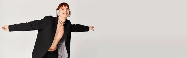 Young man in black jacket spreads his arms out in a dynamic pose against a grey studio background. — Stock Photo