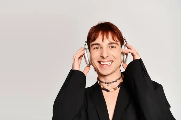 Un jeune homme élégant aux cheveux roux portant des écouteurs sur fond de studio gris. — Photo de stock