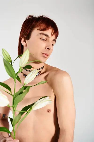 Shirtless young man holding a delicate flower in a studio against a grey background, exuding a sense of calm and beauty. — Stock Photo