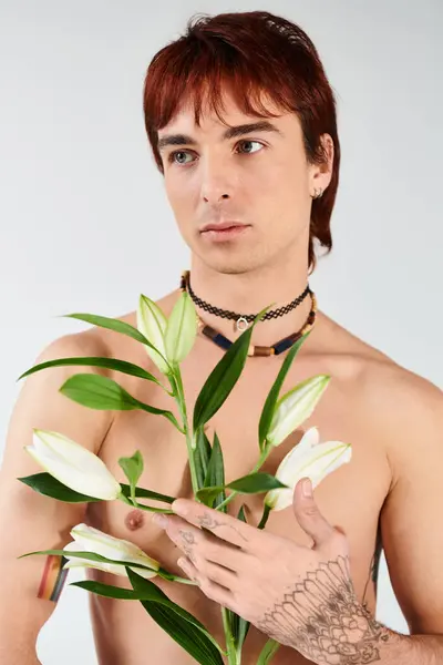 A shirtless young man in a studio holds a vibrant plant in his hand against a grey background. — Stock Photo