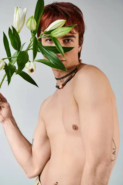 Un joven sin camisa sostiene un ramo de flores sobre un fondo gris en un ambiente de estudio. - foto de stock