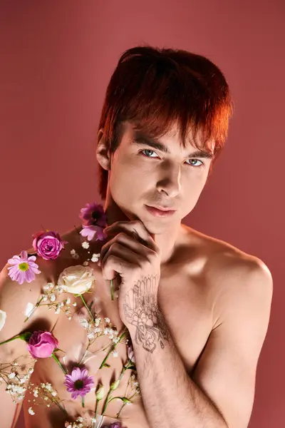 Um jovem sem camisa segurando com confiança um buquê de flores coloridas em um estúdio contra um fundo vermelho. — Fotografia de Stock