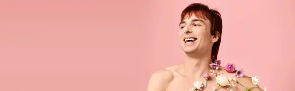A shirtless young man poses with a floral arrangement around his neck, standing against a pink studio background. — Stock Photo