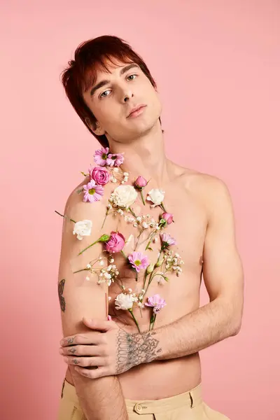 Un uomo senza camicia tiene con fiducia un mazzo di fiori colorati in uno studio con uno sfondo rosa. — Foto stock