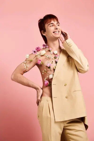 Um jovem elegante posa em um terno, adornado com flores vibrantes, contra um fundo de estúdio rosa. — Fotografia de Stock