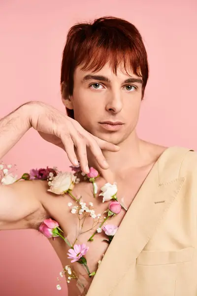 Молодой человек с рыжими волосами позирует, цветы украшают его голая грудь, установленная на фоне розовой студии. — стоковое фото