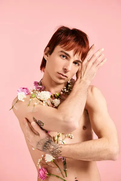 Um jovem sem camisa posa com flores ao redor de seu pescoço contra um fundo de estúdio rosa. — Fotografia de Stock