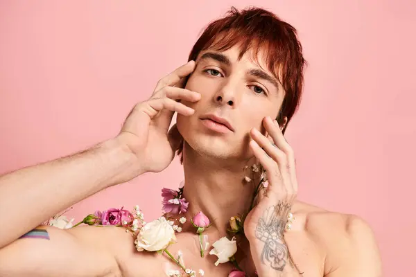 Um jovem com tatuagens no peito posa com flores em um estúdio contra um fundo rosa. — Fotografia de Stock
