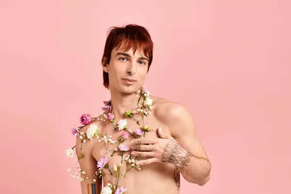 Homem sem camisa de pé com flores drapeado em torno de seu pescoço, posando em um estúdio com um fundo rosa. — Fotografia de Stock