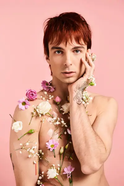 Um jovem bate em uma pose com flores em seu peito contra um pano de fundo rosa em um estúdio. — Fotografia de Stock