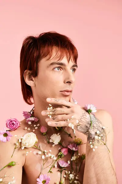 Um jovem sem camisa faz uma pose com flores coloridas espalhadas por todo o peito, contra um fundo de estúdio rosa. — Fotografia de Stock