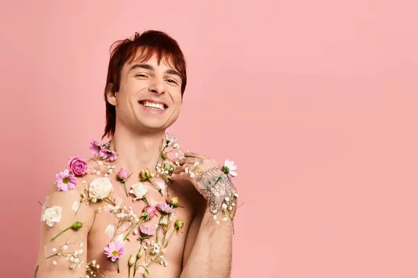 Um jovem sem camisa delicadamente posa com flores vibrantes adornando seu peito contra um fundo rosa. — Fotografia de Stock