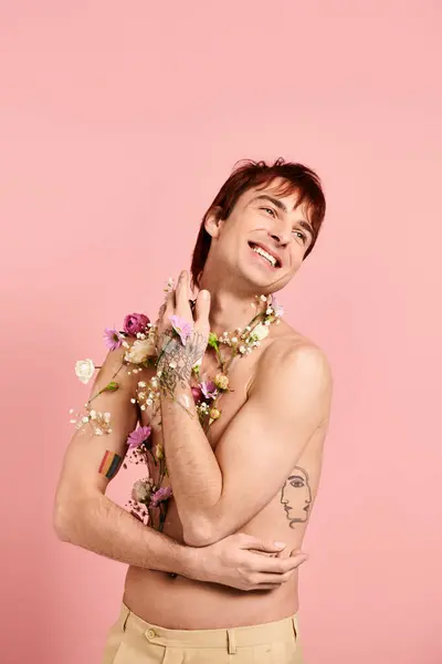 Um jovem, sem camisa, exibindo orgulhosamente flores em seu peito em um estúdio com um fundo rosa. — Fotografia de Stock