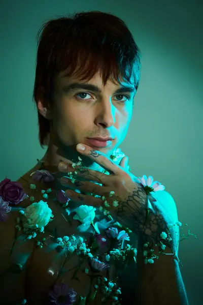 Um jovem exibe com confiança seu peito adornado com tatuagens coloridas e flores vibrantes em um estúdio contra um fundo azul. — Fotografia de Stock