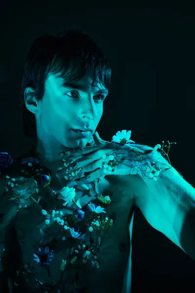 Мужчина без рубашки в окружении цветов позирует в студии с голубым светом — стоковое фото
