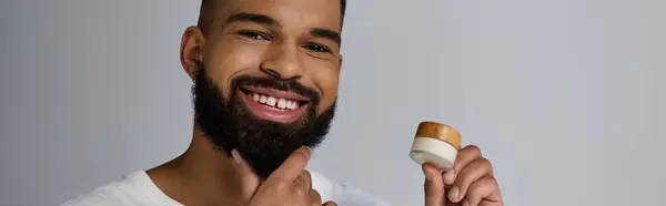 Handsome man with a beard holding a container of cream. — Stock Photo