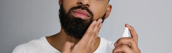 Ein gutaussehender junger Mann mit Bart, der Locion auf sein Gesicht aufträgt. — Stockfoto