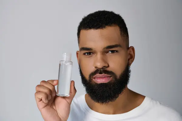 Un bel homme avec une barbe tenant une bouteille de locion. — Photo de stock