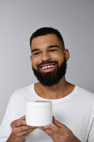 African american handsome man with a beard holding jar of cream. — Stock Photo