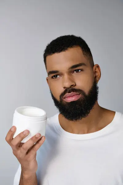 Hombre atractivo afroamericano con una barba sosteniendo tarro de crema. - foto de stock