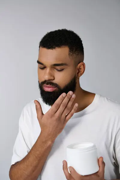 Afro-américain attrayant homme avec une barbe tenant pot de crème. — Photo de stock