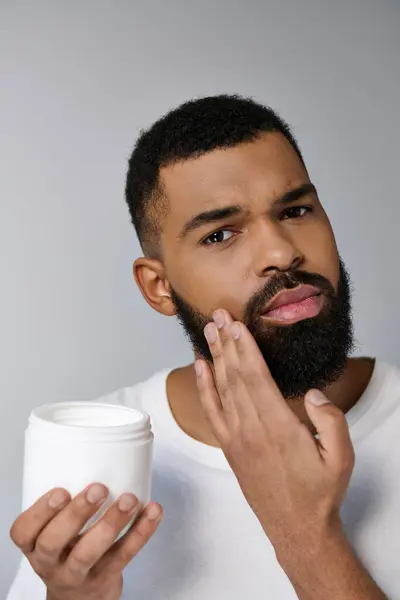 Afro-américain séduisant homme avec une barbe tenant pot de crème. — Photo de stock