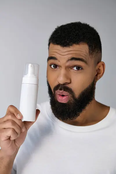 Appel jeune homme afro-américain avec une barbe tenant un tube de locion. — Photo de stock
