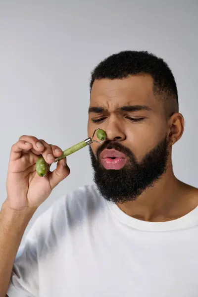 African american handsome man holds face roller for skincare routine. — Photo de stock