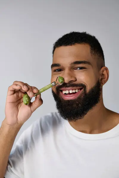 African american appealing man holds face roller for skincare routine. — Stock Photo