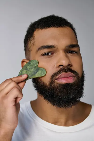 African american bearded man holds gua sha for skincare routine. — Stock Photo