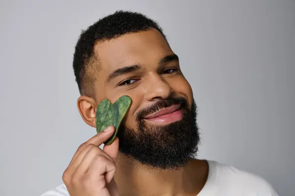 African american young man holds gua sha for skincare routine. — Stock Photo
