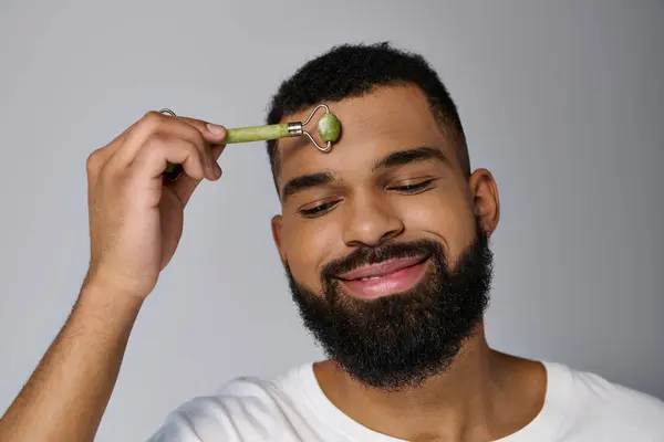 African american handsome man using face roller a for skincare routine. — Stock Photo