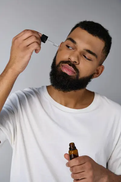 Um jovem bonito com uma barba segurando uma garrafa de óleos essenciais. — Fotografia de Stock