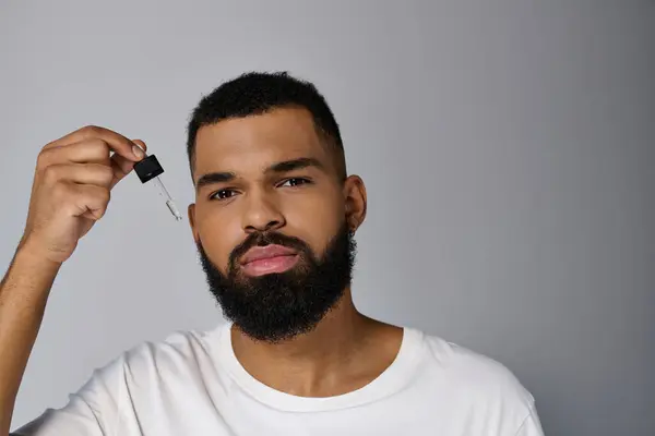 Afroamericano attraente giovane uomo con la barba in possesso di una bottiglia di siero. — Foto stock